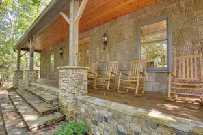 A covered porch with stone steps leading to a wooden deck, two rocking chairs, and a stone wall with a window. - Brevard Retreat w/ Hot Tub & Copper Soaking Tub (Brevard)