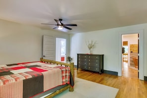 Een slaapkamer met een bed, een dressoir, een plafondventilator en een deur naar een andere kamer.
