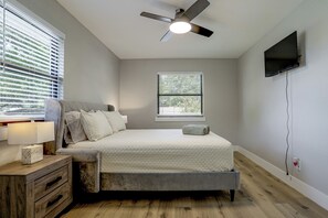 A bedroom with a bed, a ceiling fan, a window with blinds, a bedside table with a lamp, and a TV mounted on the wall. - Cozy Home Base Btwn Dallas & Fort Worth (Bedford)