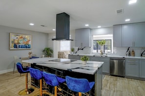 A modern kitchen with grey cabinets, a central island with bar stools, stainless steel appliances, and a large painting on the wall. - Cozy Home Base Btwn Dallas & Fort Worth (Bedford)