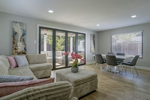 A modern living room with a sofa, ottoman, and a dining area with chairs and a table. - Cozy Home Base Btwn Dallas & Fort Worth (Bedford)