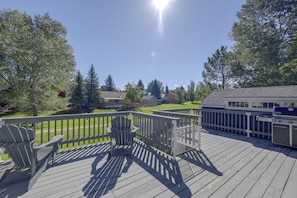 Une terrasse avec des fauteuils Adirondack et un barbecue, donnant sur une pelouse et des maisons.