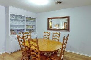 Ein Essbereich mit Holztisch und -stühlen, einem weißen Schrank mit Gläsern und einem Spiegel an der Wand.