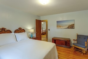 Ein Hotelzimmer mit einem großen Bett, einem Holznachttisch, einem Sessel, einem Gemälde und einer Tür zu einem weiteren Raum.