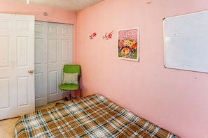 Ein Schlafzimmer mit karierter Bettdecke, einem grünen Sessel, einer weißen Tür und einer Wand mit floraler Kunst.