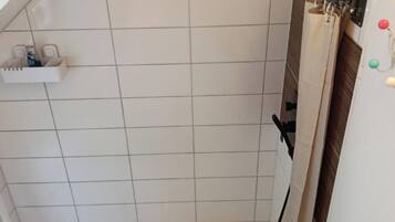 Ein Duschbereich mit weiß gefliester Wand, Ablagefläche für Pflegeprodukte und Handtuchhalter.