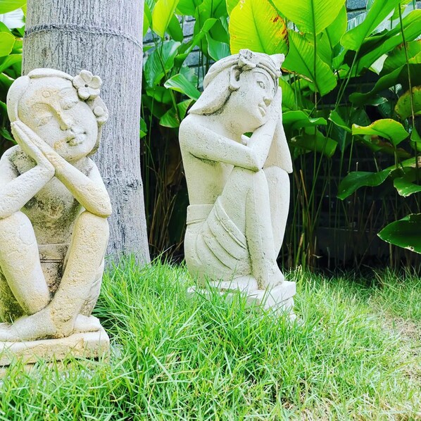 Two stone sculptures of seated figures in a garden setting.