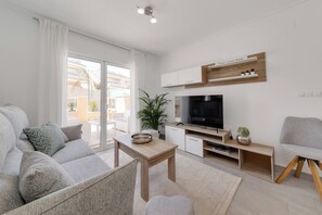 A modern living room with a sofa, a coffee table, a TV, and a balcony with a view. - CB Living - Ground floor apartment in Punta Prima (Torrevieja)