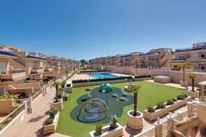 A residential complex with multiple balconies, a swimming pool, and a children's play area. - CB Living - Ground floor apartment in Punta Prima (Torrevieja)