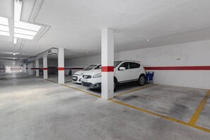 A parking garage with white pillars, yellow parking lines, and a white car parked in a bay. - CB Living - Ground floor apartment in Punta Prima (Torrevieja)