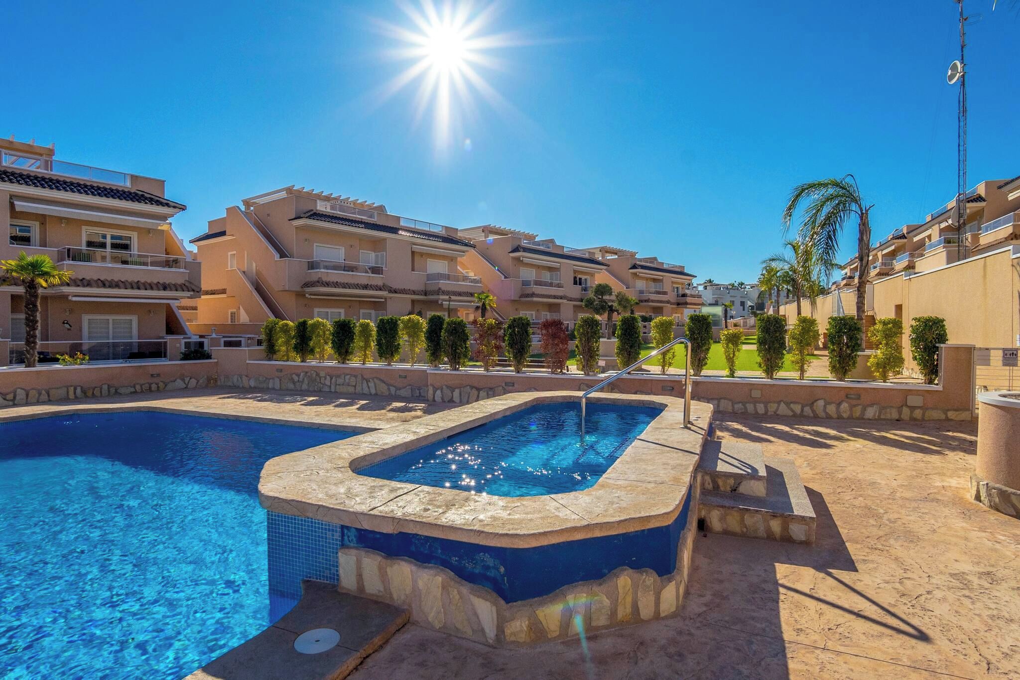 A swimming pool with a hot tub, surrounded by multi-story buildings with balconies, under a clear sky.