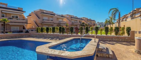 A swimming pool with a hot tub, surrounded by multi-story buildings with balconies, under a clear sky.