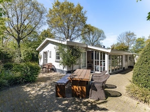 A white building with a covered patio area, a wooden bench, and a wicker chair. - Holiday Home With 2 Bedrooms (Oostkapelle)