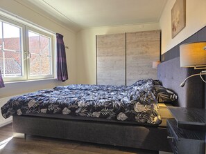 Ein Schlafzimmer mit Bett, Nachttisch, Kleiderschrank und einem Fenster mit Vorhängen.