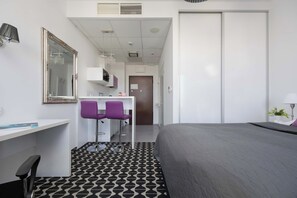 Ein Hotelzimmer mit Bett, Schreibtisch mit Stuhl, Spiegel und einer Küchenzeile.