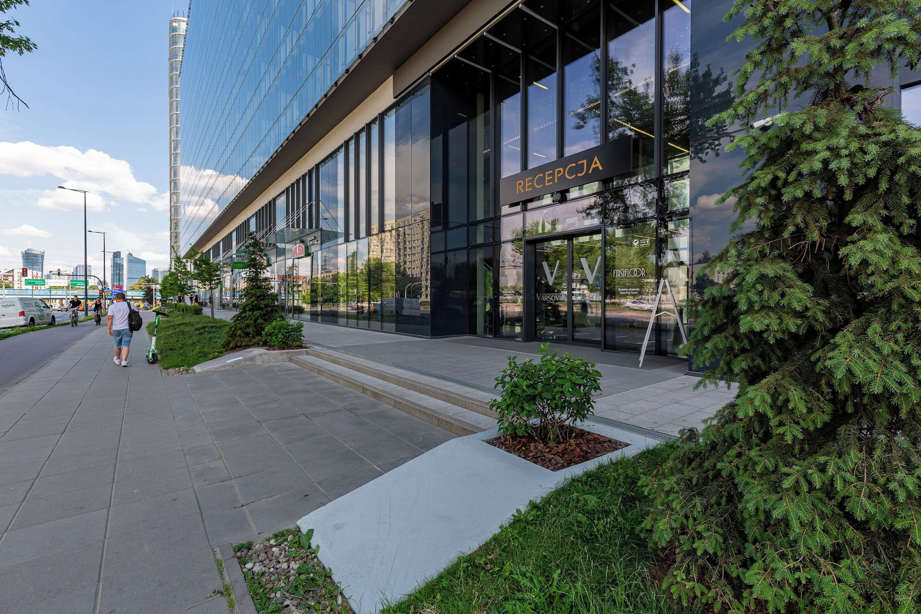 A modern building with a reception area, glass facade, and a clear sky.