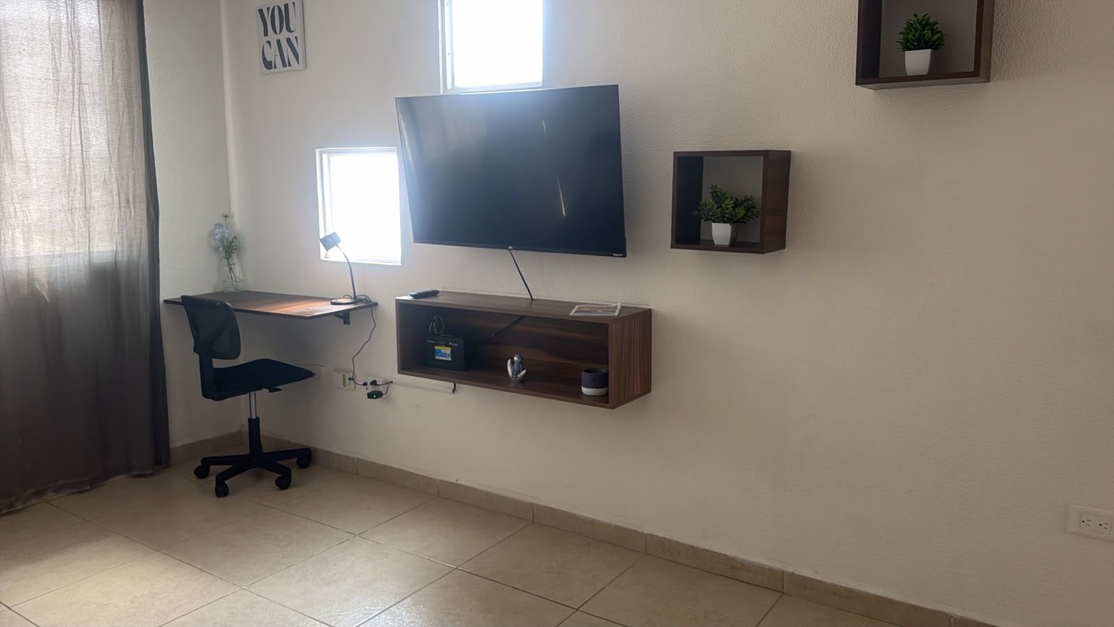 A room with a desk, chair, TV, and shelves.