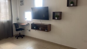 A room with a desk, chair, TV, and shelves.