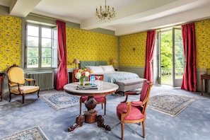 A bedroom with floral wallpaper, a bed, a round table with a vase, and two chairs.