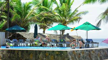 Un área de piscina con sillas de descanso y sombrillas, rodeada de palmeras.