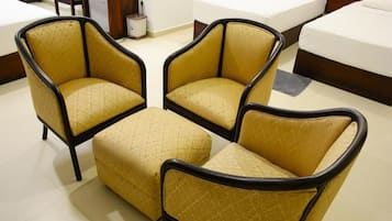 A hotel room with three armchairs and a matching ottoman, a bed with white bedding, and a small table with a lamp.