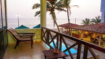 Un balcón con vista al mar, una piscina y un área de restaurante.