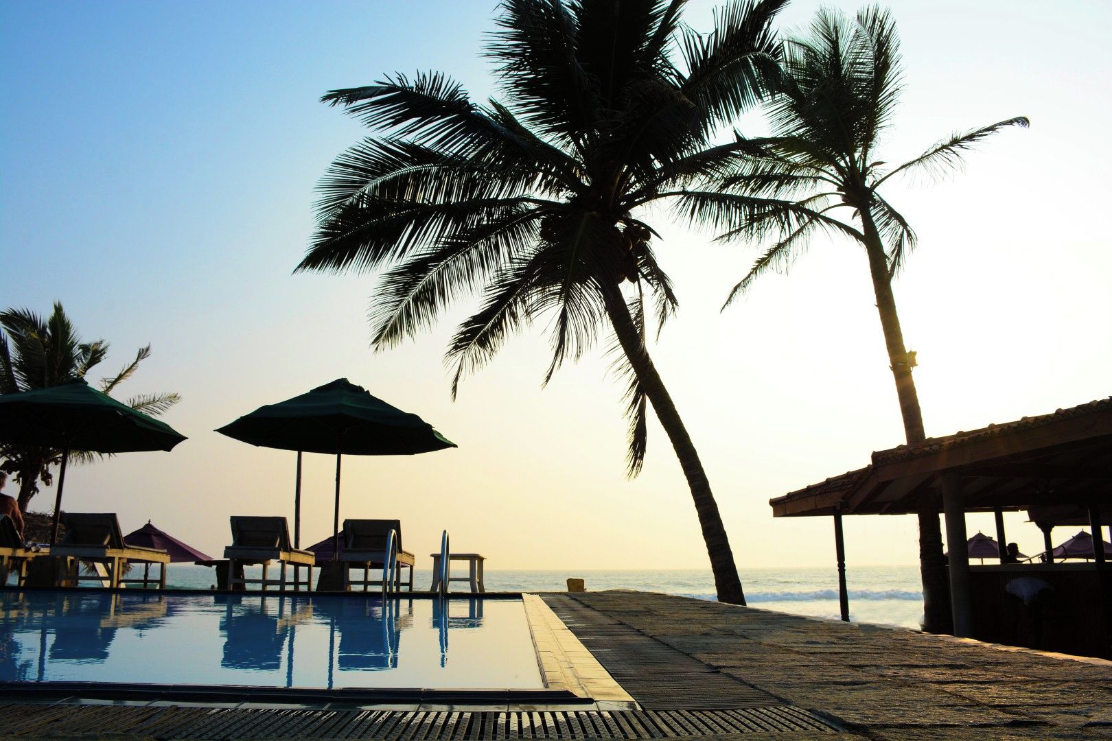 Área da piscina com espreguiçadeiras e guarda-sóis, com vista para o oceano.