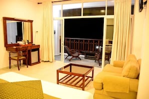A hotel room with a balcony, a sofa, a desk with a chair, and a large mirror. - Hikka Bliss (Hikkaduwa)