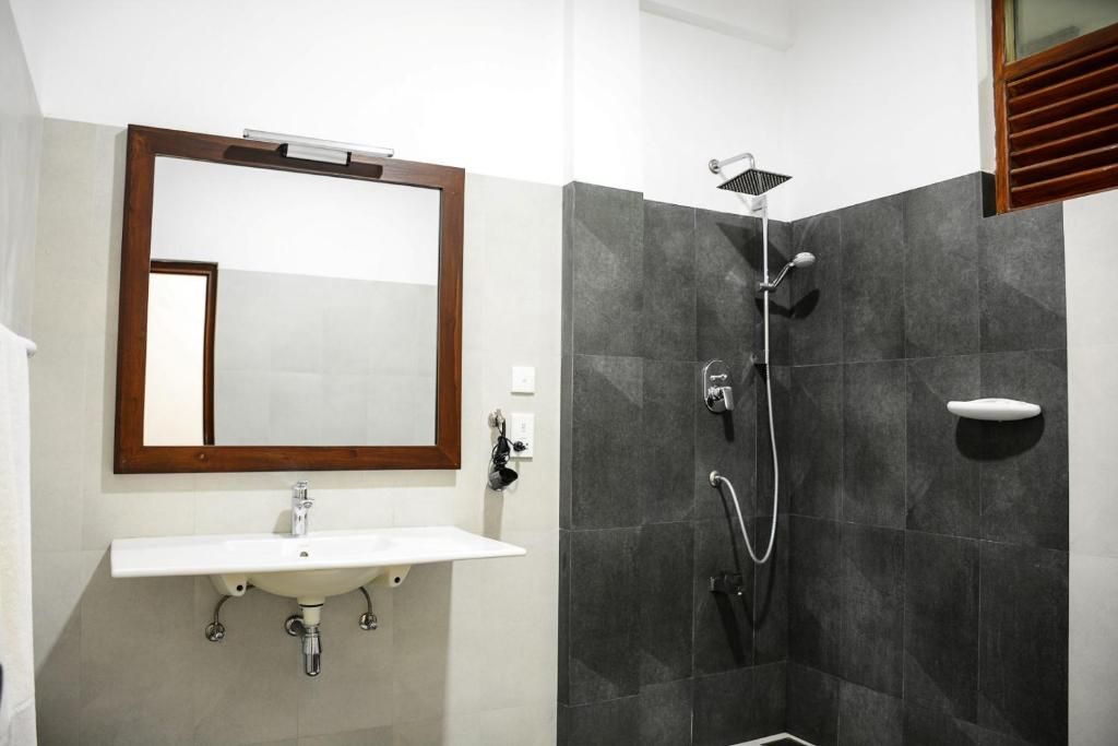 A bathroom with a white sink, a mirror, and a shower with a handheld showerhead.