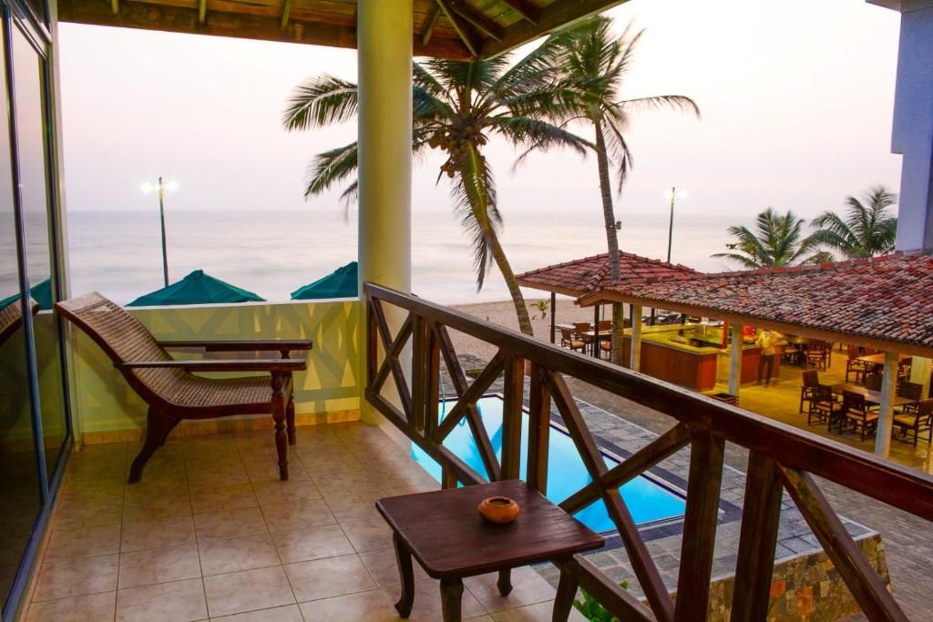 A balcony with a view of the sea, a pool, and outdoor seating.