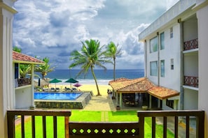 A view from a balcony overlooking a pool, beach, and ocean with palm trees. - Hikka Bliss (Hikkaduwa)