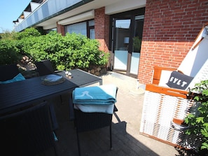 Eine Terrassengruppe im Freien mit Tisch, Stühlen und einem Schild mit dem Wort 'SYLT'.