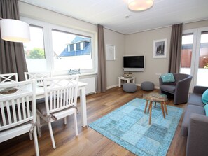 Ein modernes Wohnzimmer mit einem weißen Babybett, einem grauen Sofa, einem Glastisch und einem blauen Teppich.
