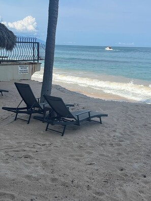 A beach with two lounge chairs, a palm tree, and a sign indicating private property with no trespassing. - Brisaazul Oceanfront 2BR (Puerto Vallarta)
