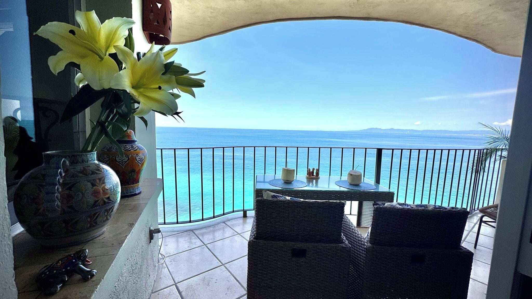 A balcony with a view of the sea, wicker furniture, and decorative vases.
