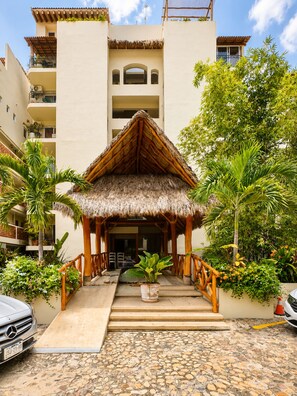 A resort with a thatched-roof structure, a paved entrance, and a stone-tiled driveway. - Brisaazul Oceanfront 2BR (Puerto Vallarta)