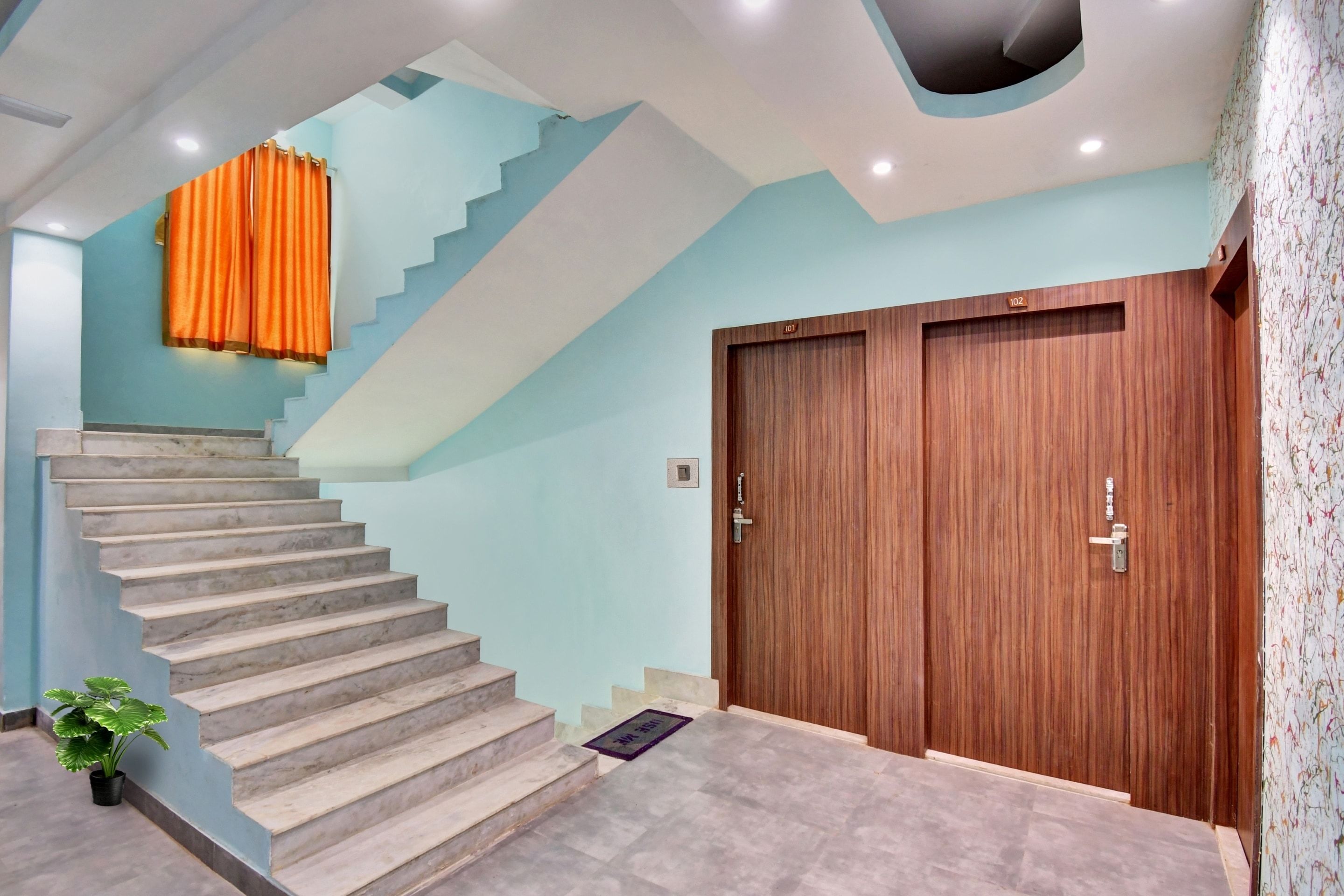 A staircase leading to a wooden door with a number plate, a potted plant, and a wall with a geometric pattern.