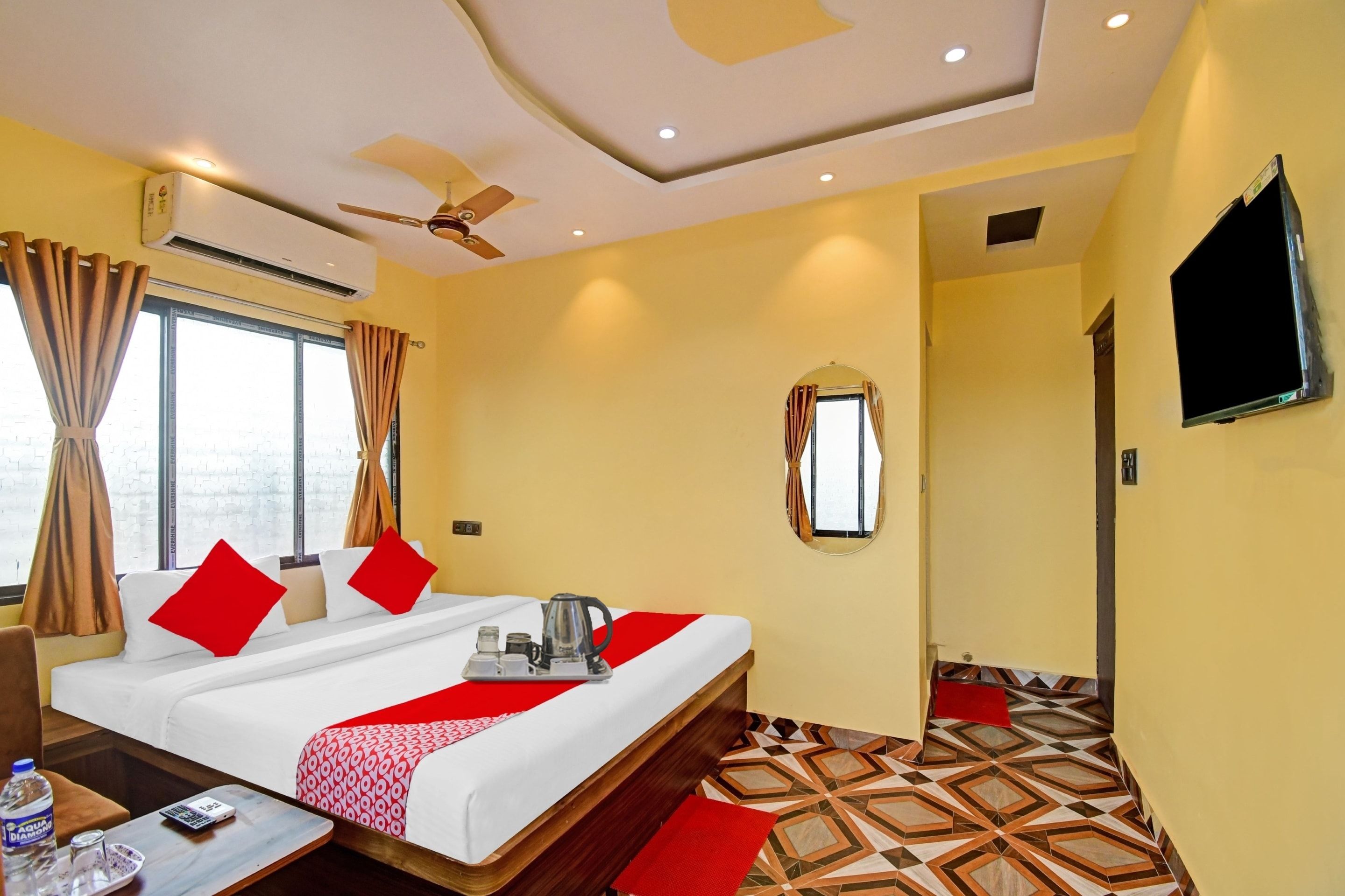 Una habitación de hotel con cama, televisor, ventilador de techo y ventana con cortinas.