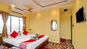 Una habitación de hotel con cama, televisor, ventilador de techo y ventana con cortinas.