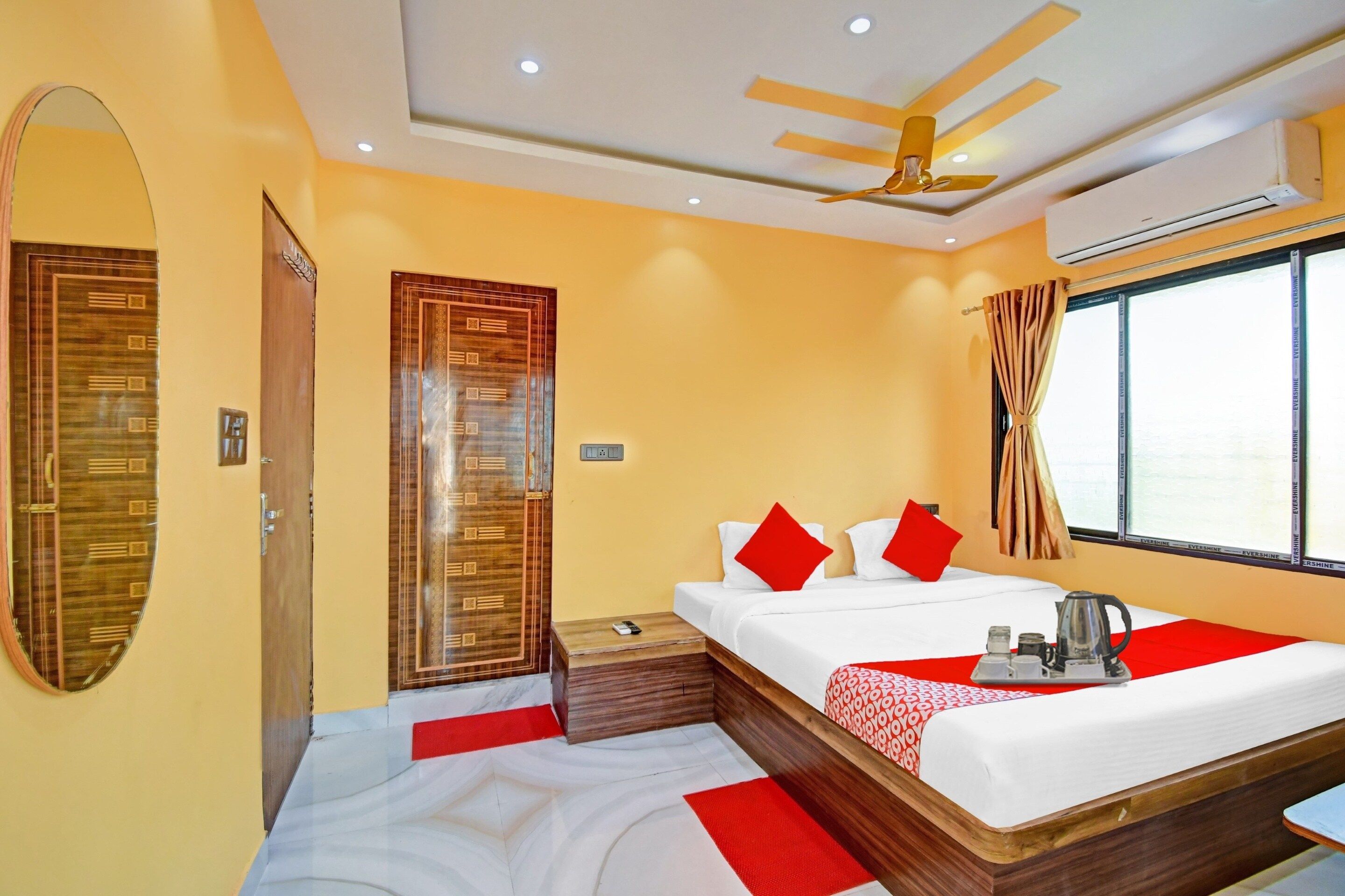 A hotel room with a bed, a ceiling fan, a window with curtains, and a mirror.