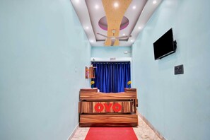 Un área de recepción con un mostrador de madera identificado con 'OYO', un ventilador de techo, un televisor de pantalla plana y una cortina azul.
