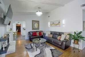 Sala de estar com sofá, mesa de centro e televisão. Escada leva a outro cômodo.