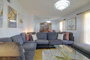 Un salon avec un canapé d’angle, une table basse en verre et un lustre.