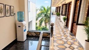 Un pasillo de hotel con dispensador de agua, plantas en macetas y piso estampado.