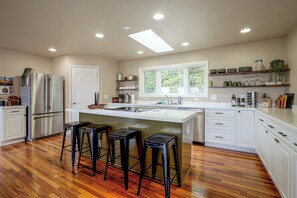 A modern kitchen with a central island, bar stools, a refrigerator, and built-in shelves. - River Views & Gas Fire Table: Maiden Rock Retreat (Maiden Rock)