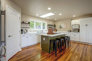 A modern kitchen with white cabinetry, a central island with stools, and a large window providing natural light. - River Views & Gas Fire Table: Maiden Rock Retreat (Maiden Rock)
