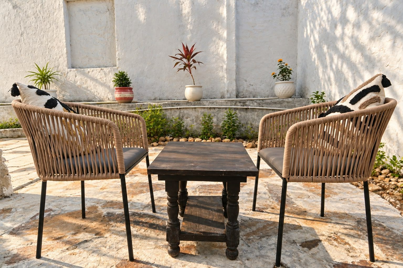 Un patio con due poltrone in vimini, un tavolo in legno e piante in vaso.
