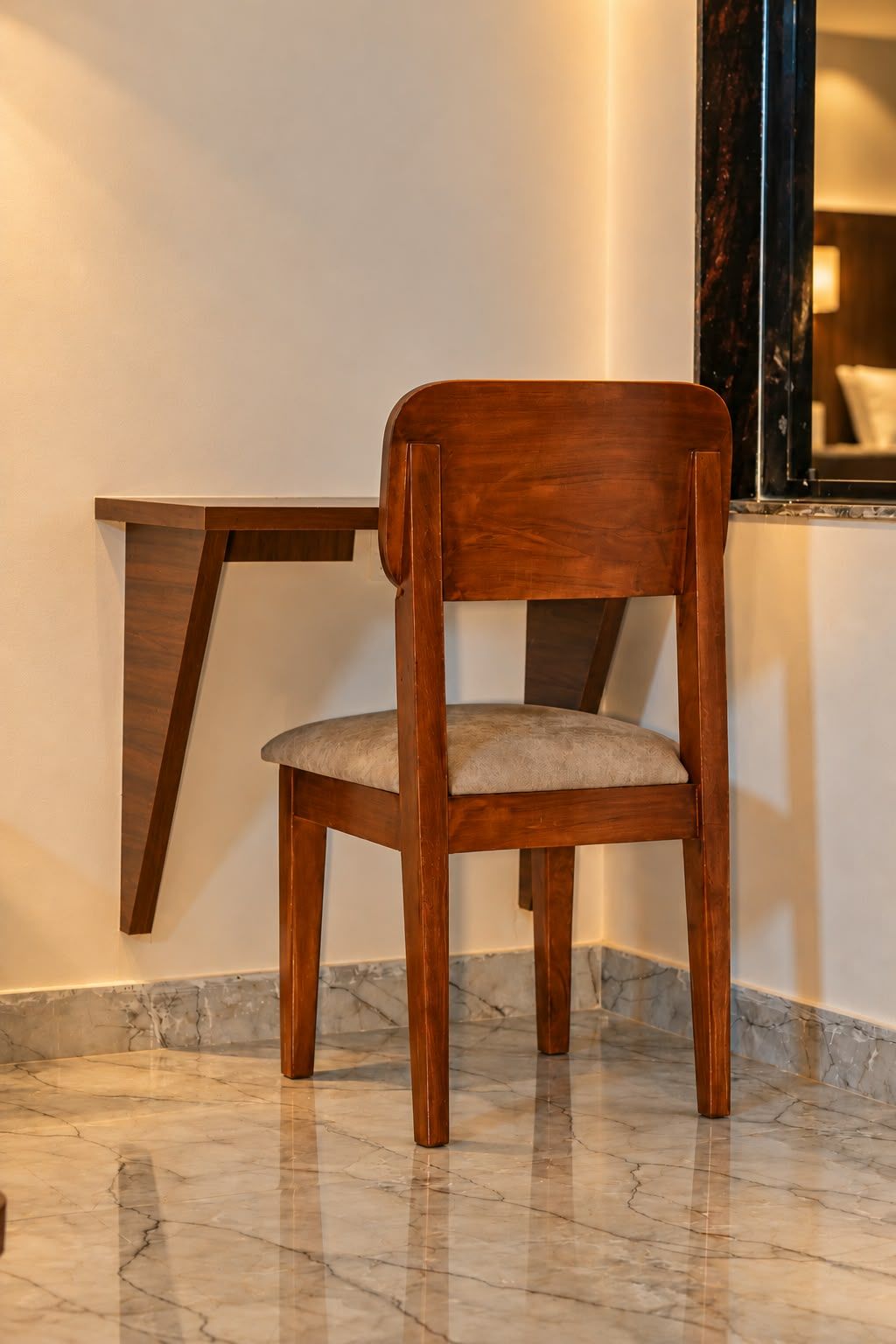 Una sedia in legno con seduta e schienale imbottiti, posizionata davanti a un pavimento in marmo e a una mensola in legno fissata al muro.