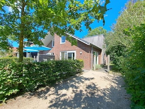 A residential property with a gravel driveway, a brick house, and a blue umbrella. - Holiday Home With 3 Bedrooms (Sint Maartensvlotbrug)