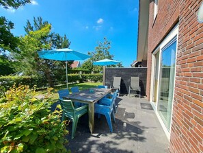 An outdoor patio with a table and chairs, two blue umbrellas, and a brick wall. - Holiday Home With 3 Bedrooms (Sint Maartensvlotbrug)